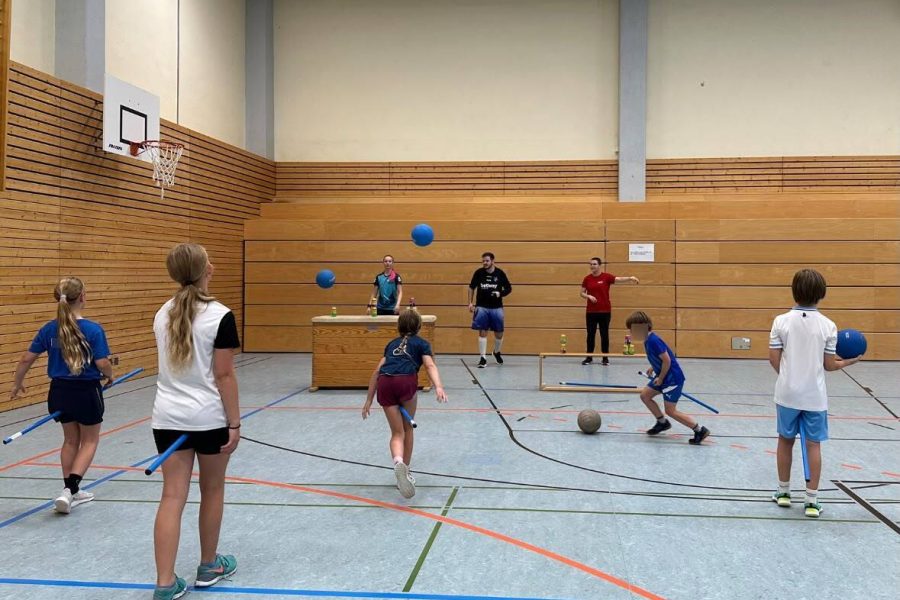 Kidditch Kinder werfen mit Bällen auf Dosen in einer Turnhalle